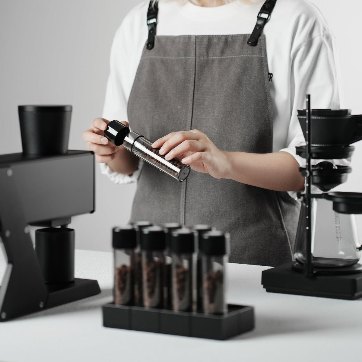MHW-3BOMBER C6678T clear single bottle being uncapped by a barista; other bottles, beans, stand and grinder are display props, not included.