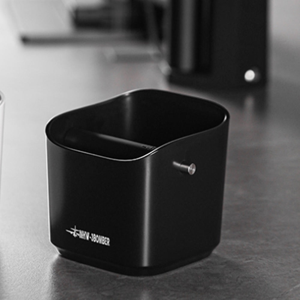 MHW-3BOMBER GB5967B black square knock box on a coffee counter, reverse angle showing the knock-bar fitting; background equipment is not included