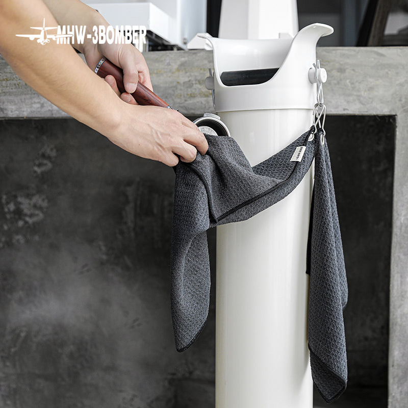 MHW-3BOMBER black hangable towel held beside its hanging attachment