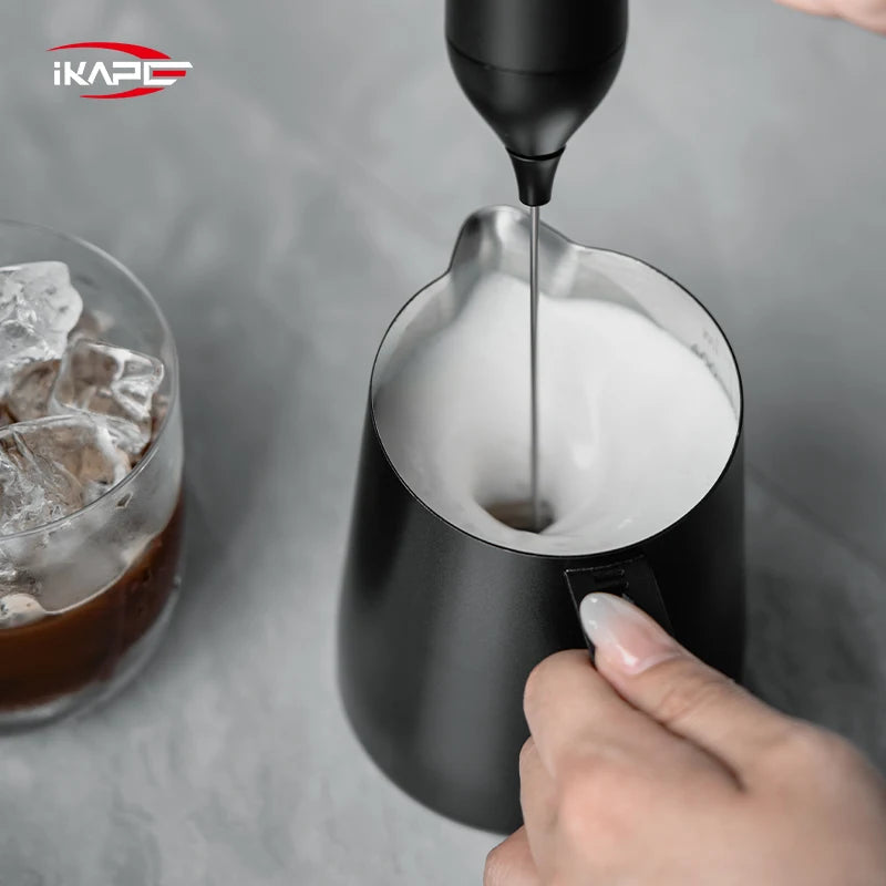 Black IKAPE hollow-handle milk pitcher used with a handheld milk frother