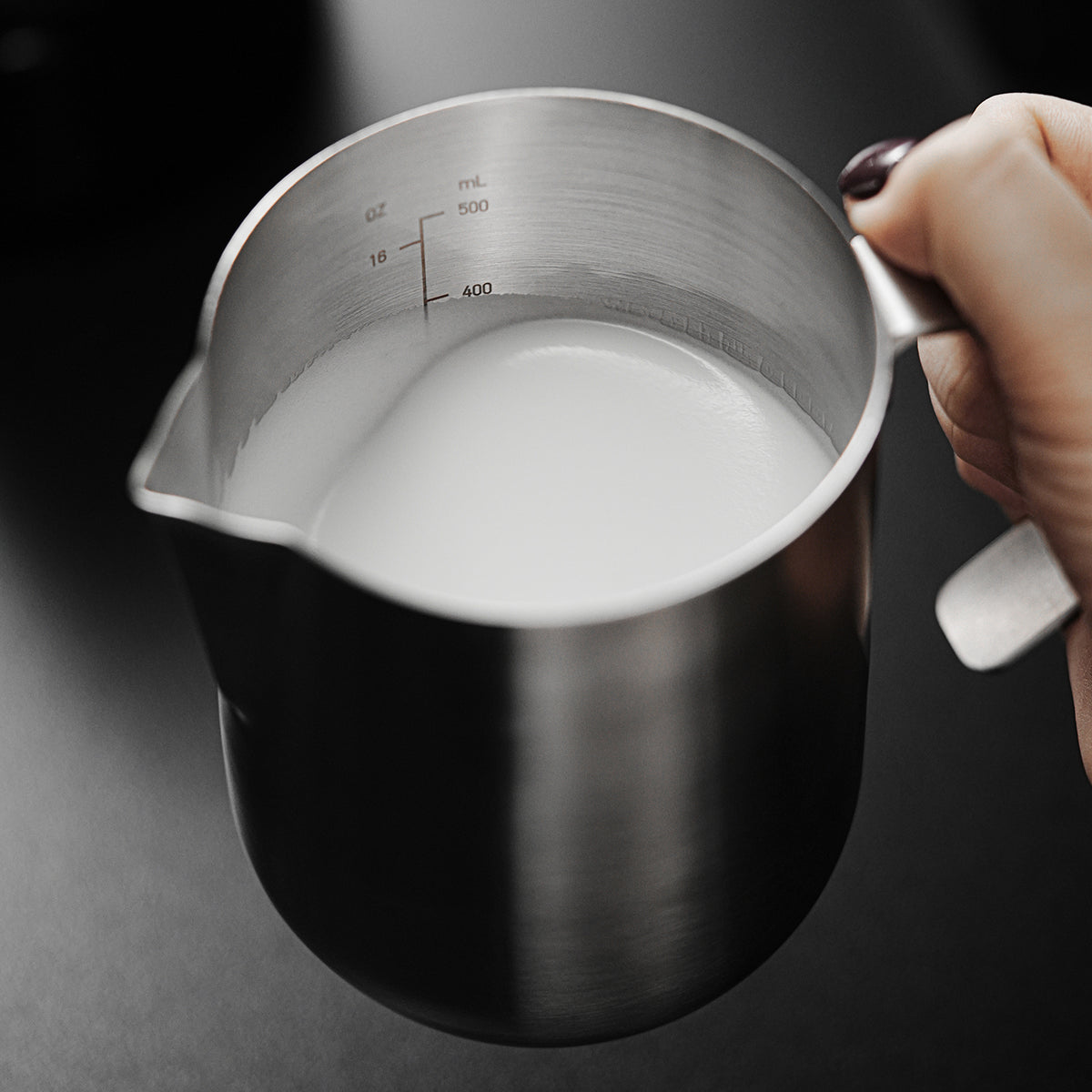MHW-3BOMBER P5521 600 ml Silver Magician steaming pitcher containing milk, showing the rounded body, open side handle and printed fill marks