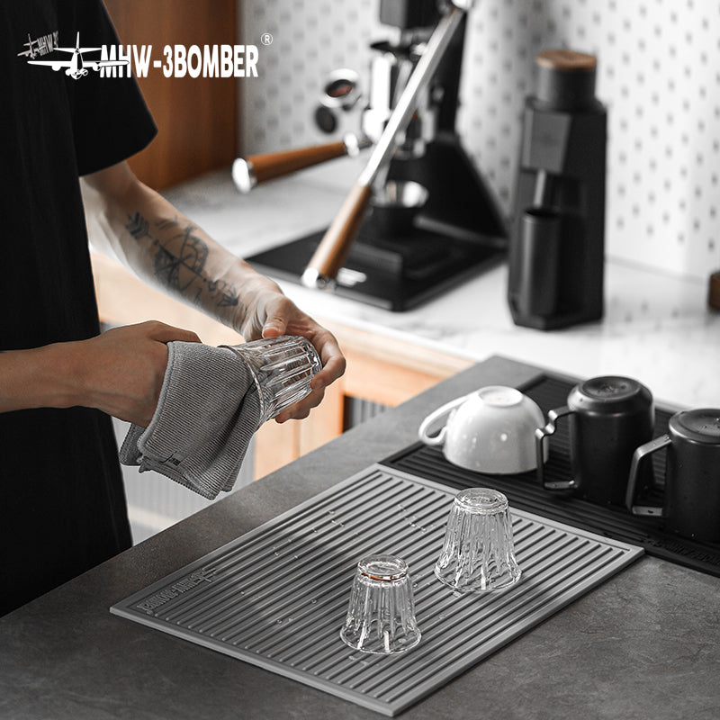 MHW-3BOMBER SP5325G Light Grey dish drying pad with ribbed surface at a coffee station; glasses and equipment not included.