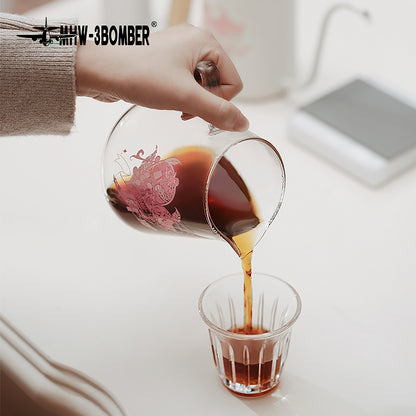 G5199P Heartbeat artwork server pouring into a glass on a grey counter with a beige sleeve visible. Other pictured tools, coffee and props are not included.