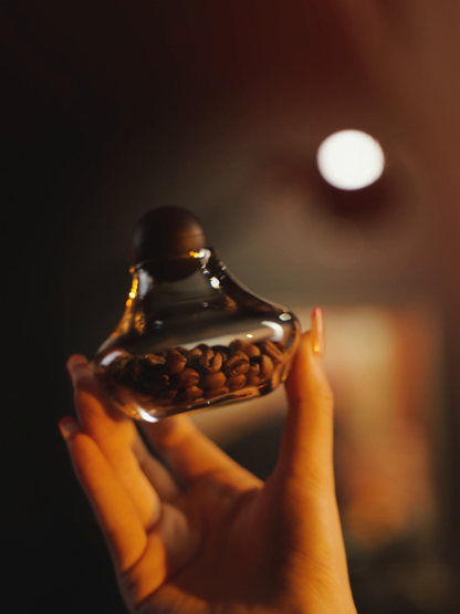 MHW-3BOMBER G6524 glass Coffee Display Jar with its silicone lid held in hands; coffee beans are display props