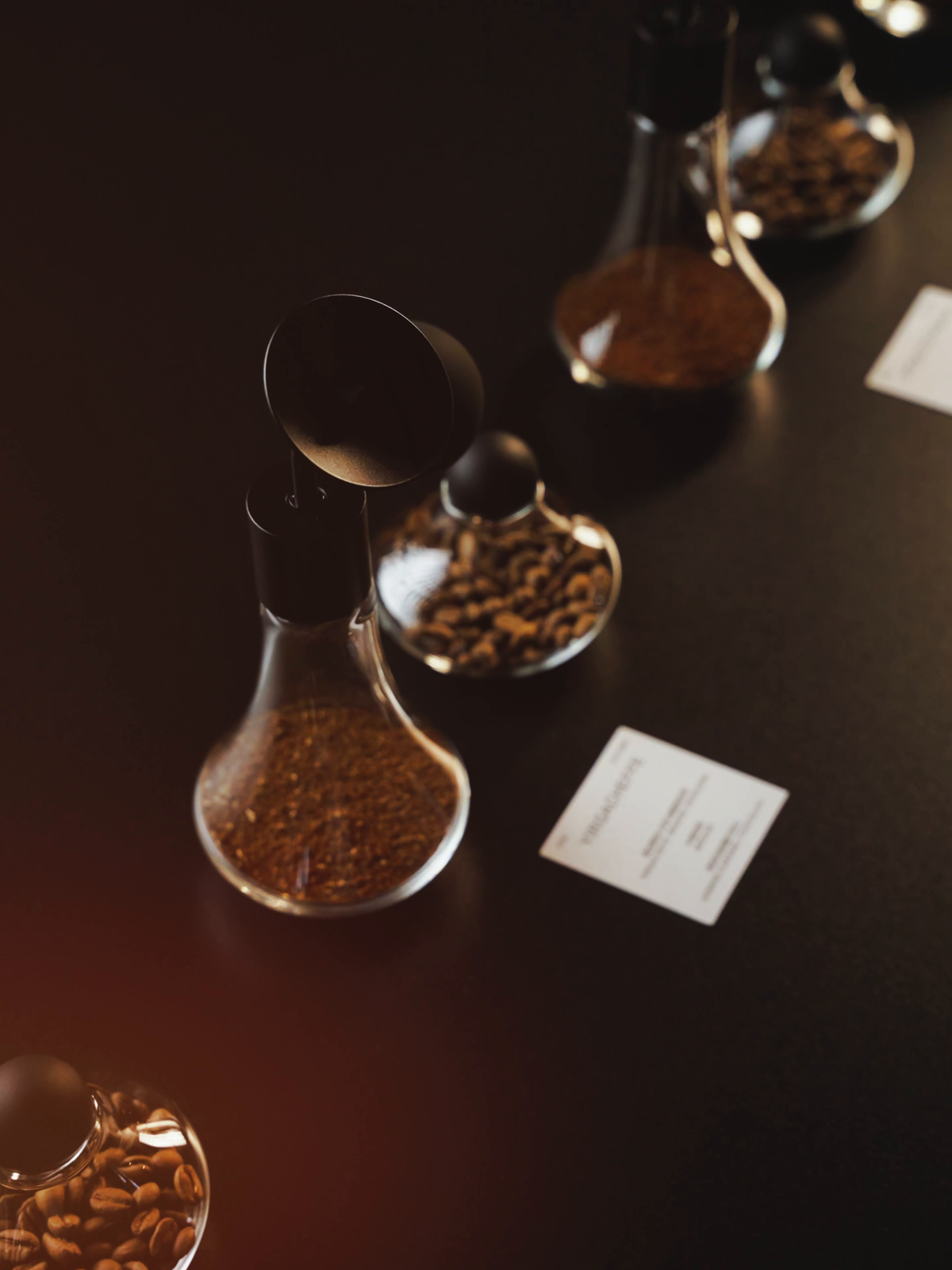 MHW-3BOMBER G6524 Coffee Display Jars arranged on a coffee tasting table; aroma bottles and coffee beans are separate display props