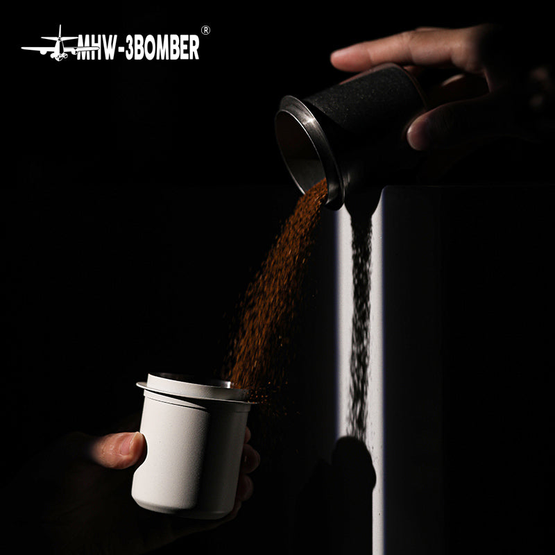 MHW-3BOMBER Black DC5615B dosing cup pouring grounds into a white receiving cup; receiving cup is a prop
