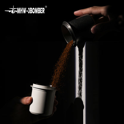 MHW-3BOMBER Black DC5615B dosing cup pouring grounds into a white receiving cup; receiving cup is a prop