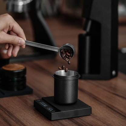 MHW-3BOMBER Black DC5615B dosing cup receiving beans on a scale; scale and scoop are props