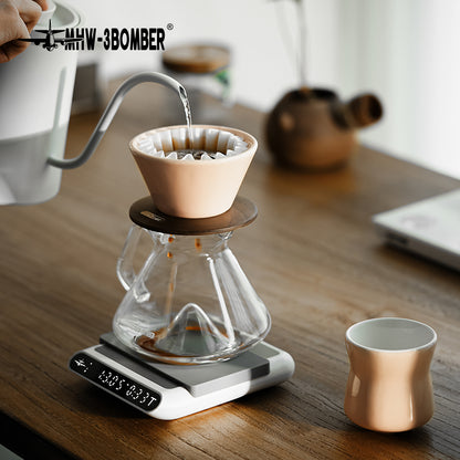 MHW-3BOMBER Lotus Pink dripper on a glass server during pouring; server, cup, kettle and scale are reference props