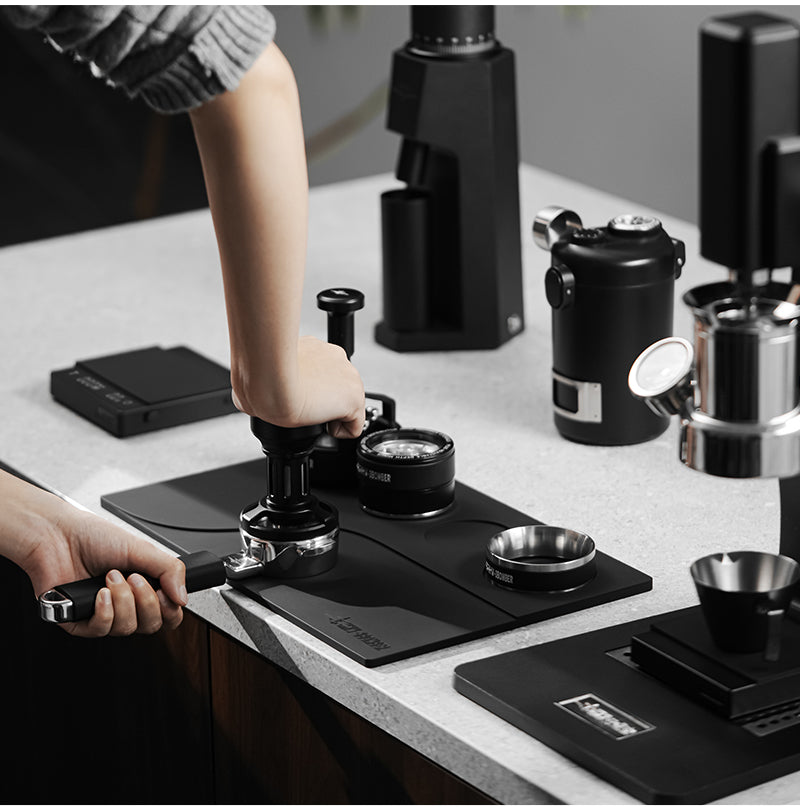 MHW-3BOMBER Black Yu mat supporting a tamping demonstration; espresso tools are reference props