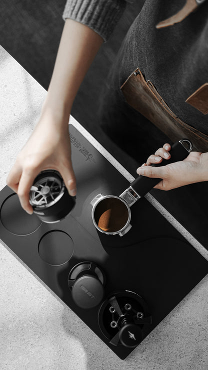 MHW-3BOMBER Black recessed Yu mat during portafilter preparation at a workstation; tools not included