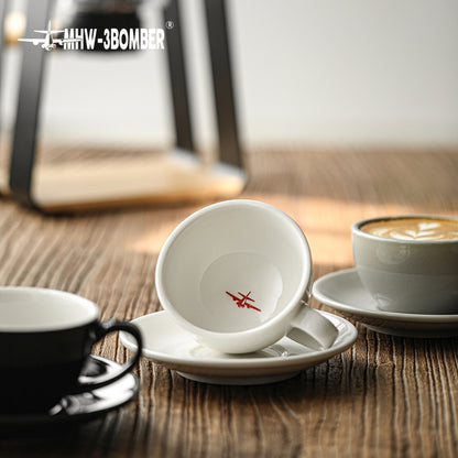 MHW-3BOMBER C5080W Beige White 280 ml latte cup tilted on its saucer, showing the interior logo; other cups are photo props.