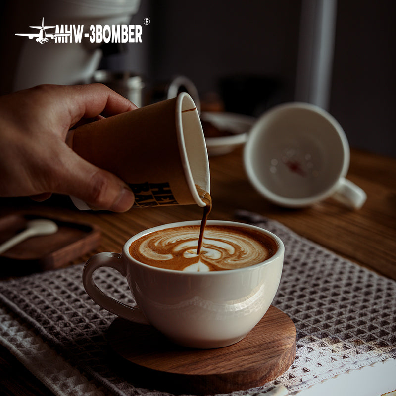 MHW-3BOMBER C5080W Beige White 280 ml latte cup during a coffee-pouring demonstration; jug and wooden coaster are photo props.