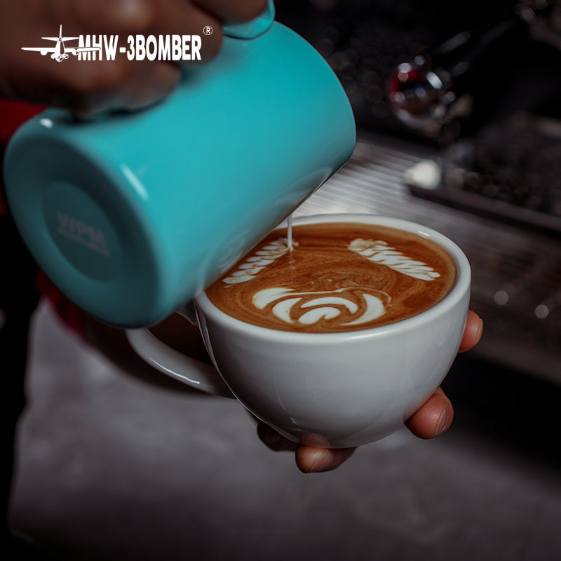 MHW-3BOMBER C5080W Beige White 280 ml latte cup held during milk pouring; turquoise pouring vessel is a photo prop.