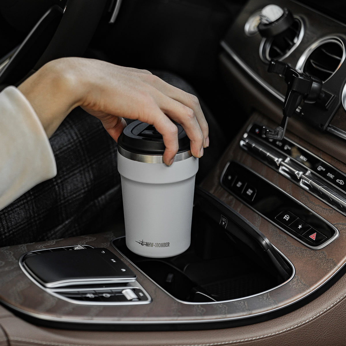 MHW-3BOMBER M5716W Cooki 360 ml travel cup: beige-white cup held in a car setting; other pictured equipment and props are not included.