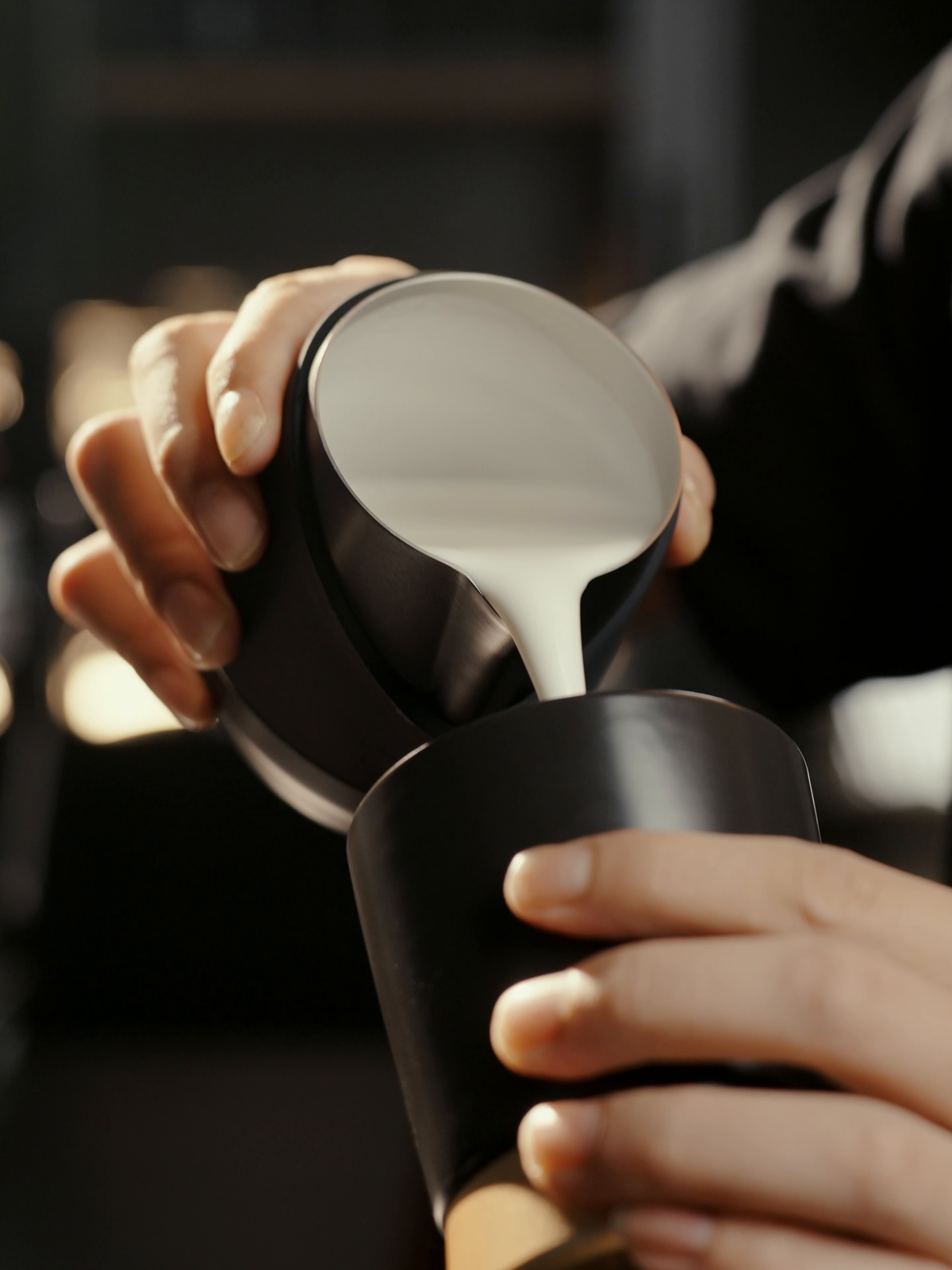 MHW-3BOMBER P6513B black 400 ml GT Handleless Milk Pitcher pouring latte art into a black cup; cup is not included