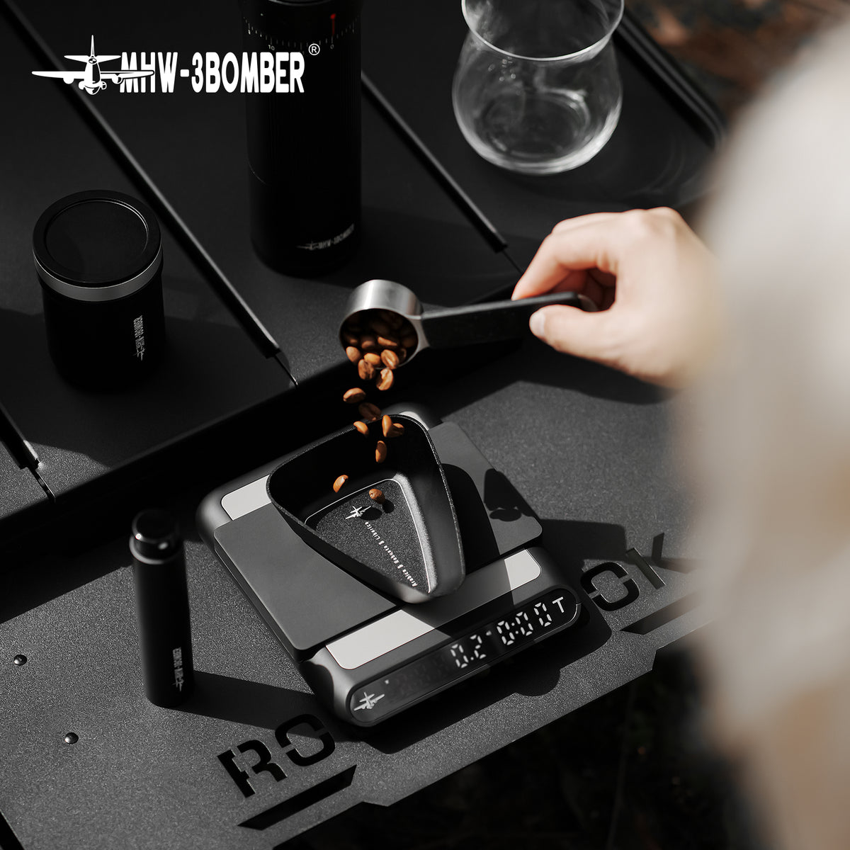 MHW-3BOMBER P6562B small black BeanBoat tray receiving coffee beans on a scale; scale, spoon and coffee are demonstration props