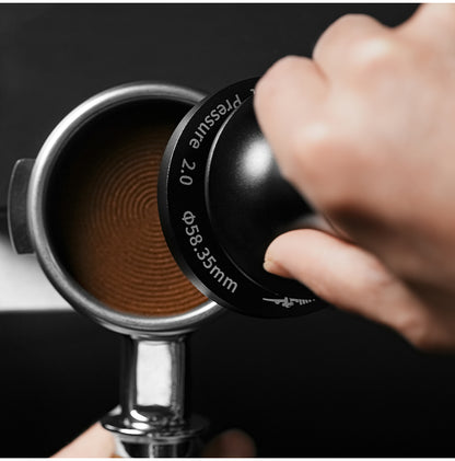 MHW-3BOMBER T6172T 58.35 mm ripple-base tamper in use; the ring marking and concentric coffee imprint are visible