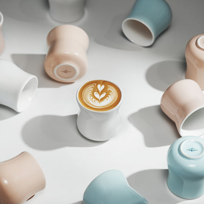 Ice Satin White wide-rim Aura cup with latte art in the centre of an overhead cup arrangement. Other cups and coffee are presentation props.