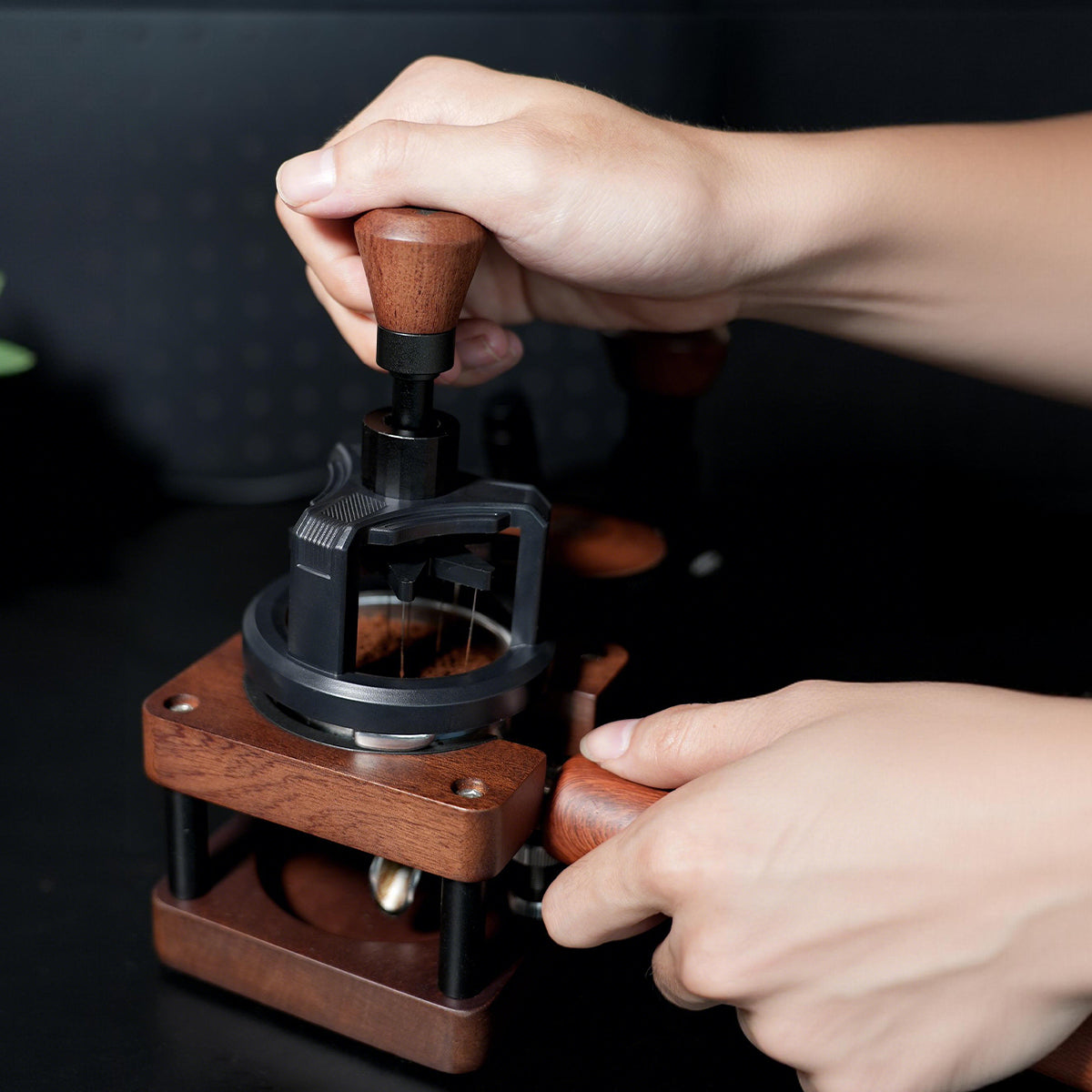 HiBREW Rotary 58mm WDT tool — two hands operating the wooden rotary grip and supporting a tamping station; pictured portafilter, coffee and station are demonstration props, not included.