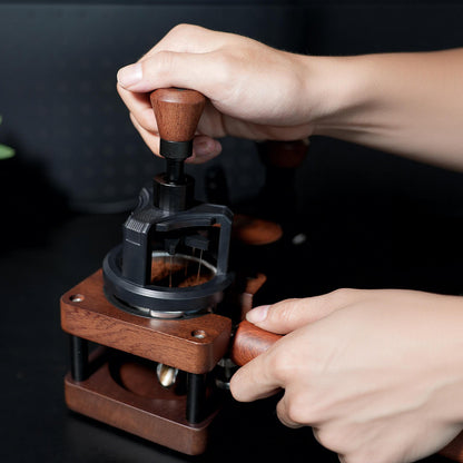 HiBREW Rotary 58mm WDT tool — two hands operating the wooden rotary grip and supporting a tamping station; pictured portafilter, coffee and station are demonstration props, not included.