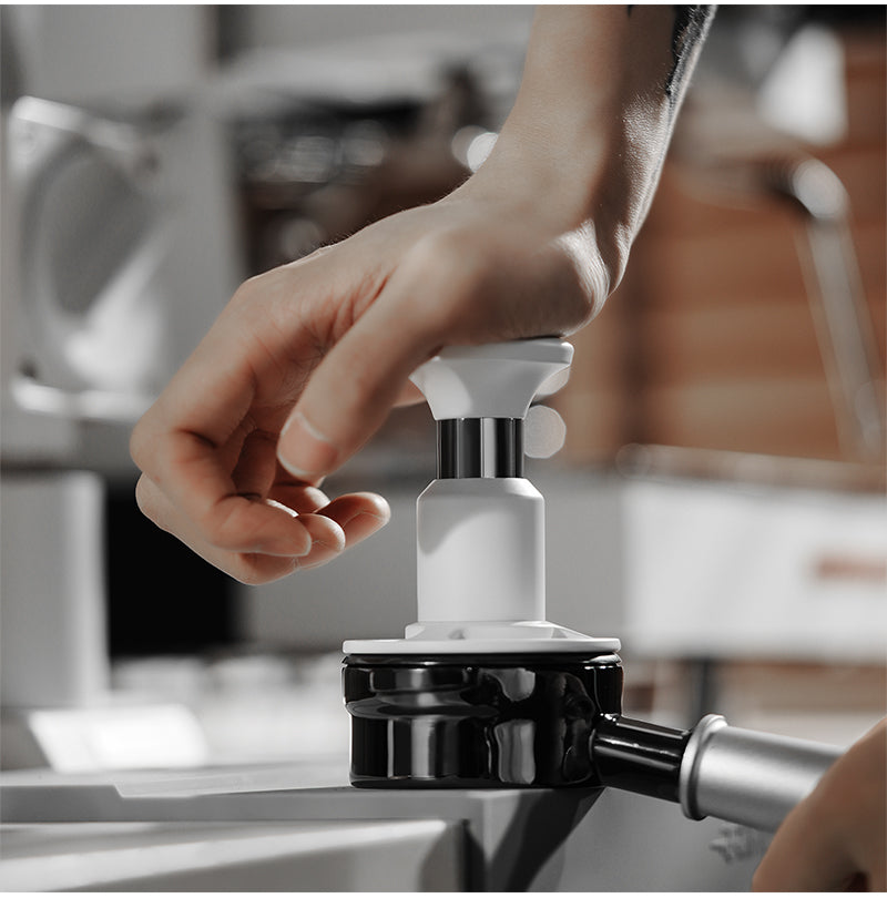 White 58.35 mm Knight Impact Tamper pressing a basket; portafilter and station are photo props