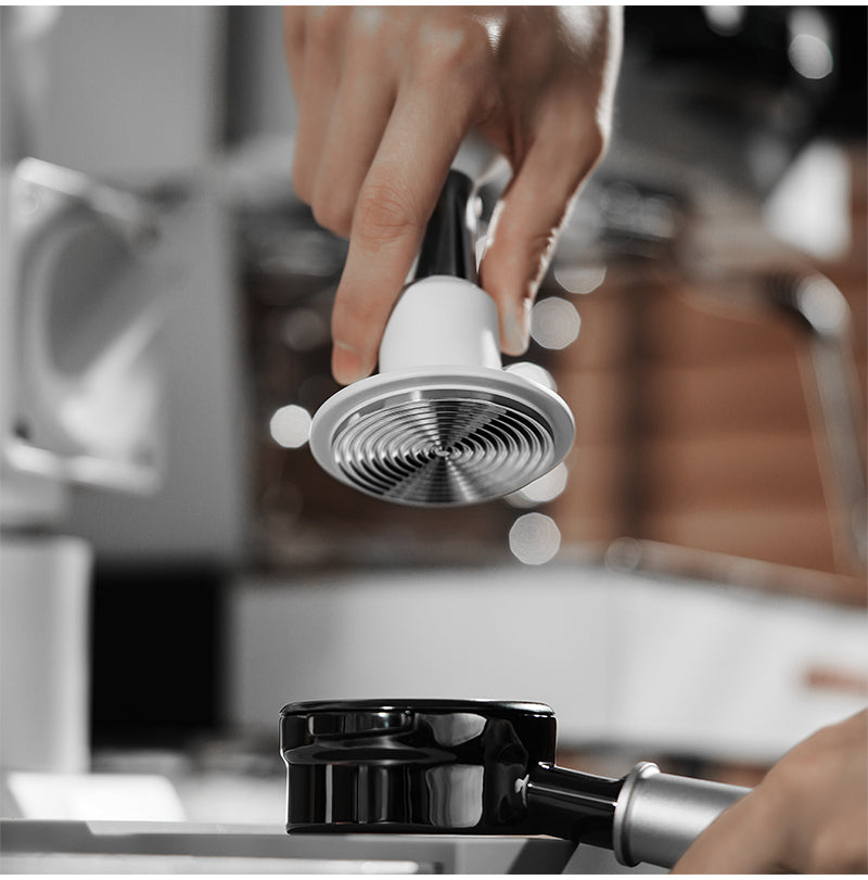 White 58.35 mm Knight Impact Tamper ripple underside held above a basket; portafilter is a photo prop