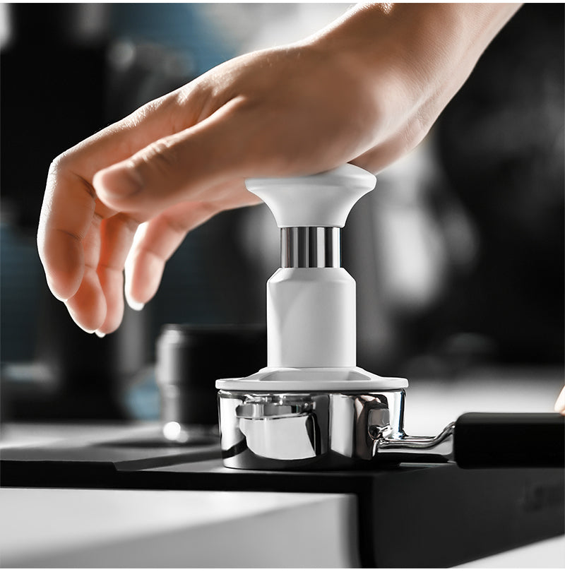 White 58.35 mm Knight Impact Tamper operating view on a stainless portafilter; portafilter and station are photo props