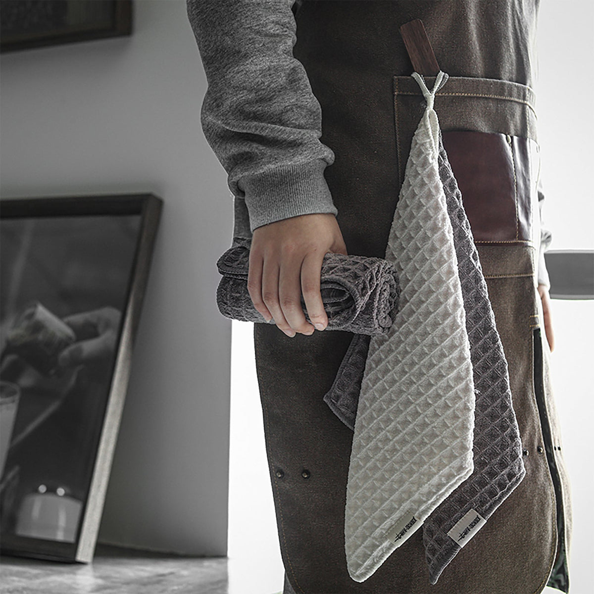 MHW-3BOMBER beige-white and dark-grey square waffle towels hung from an apron; several towels shown for comparison, one selected SKU per purchase.