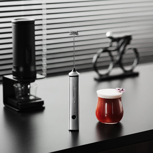 MHW-3BOMBER MF6834S silver handheld frother standing beside a drink; glass and grinder not included