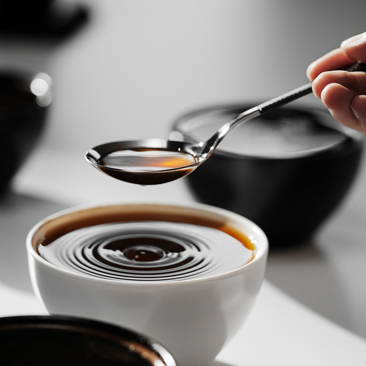MHW-3BOMBER S5706S black-handle silver-bowl cupping spoon held over a coffee cup; other items are scene props