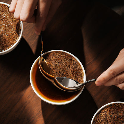 MHW-3BOMBER S5706S black-handle silver-bowl spoon on the right skimming coffee beside a gold comparison spoon; gold spoon and cup are not included