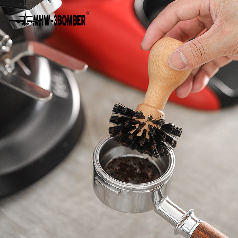MHW-3BOMBER B5341 beech basket brush held above a portafilter basket; espresso machine is a scene prop
