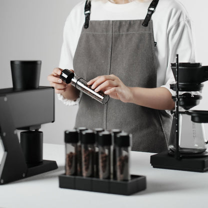 MHW-3BOMBER C6678T clear single bottle being uncapped by a barista; other bottles, beans, stand and grinder are display props, not included.