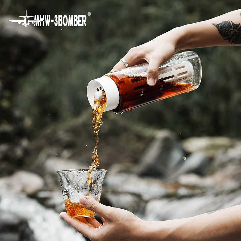 MHW-3BOMBER CE6136 White cold-brew pot pouring over a serving glass outdoors; scene tools, glasses and drink ingredients are not included.
