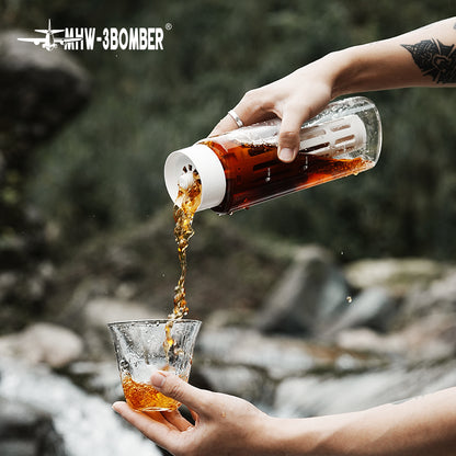 MHW-3BOMBER CE6136 White cold-brew pot pouring over a serving glass outdoors; scene tools, glasses and drink ingredients are not included.