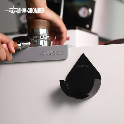 DPH5713B Black droplet holder on counter edge with tamping action in background; tamper, mat, machine and portafilter not included