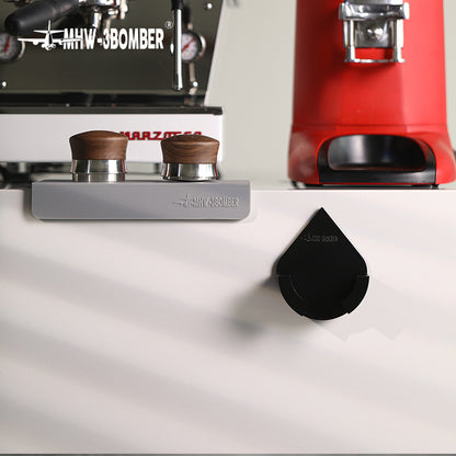 DPH5713B Black droplet holder empty on counter edge beside espresso preparation tools; other equipment not included