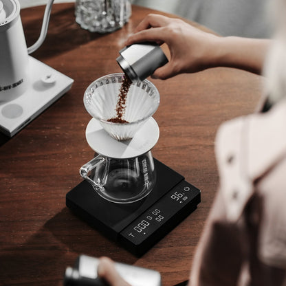 MHW-3BOMBER ES5663 black Cube Coffee Scale 3.0 Pro Max during coffee-dose preparation for pour-over; dripper, server and dosing cup are separate props