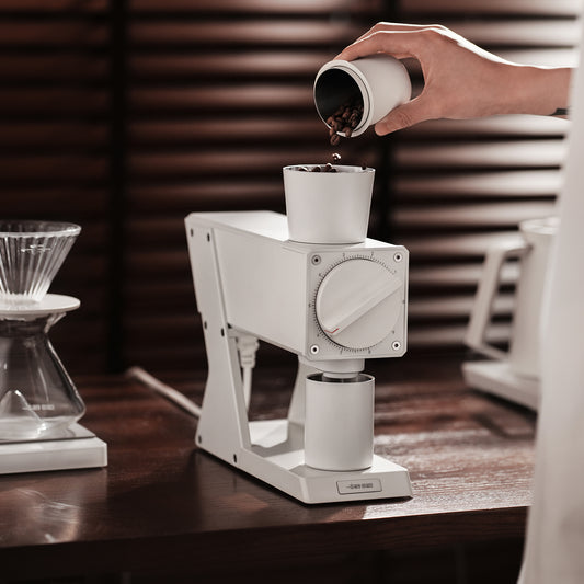White F74 Navigator grinder while beans are poured into its hopper; brewing props not included.