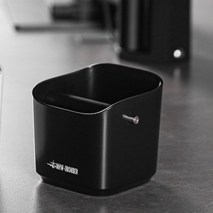 MHW-3BOMBER GB5967B black square knock box on a coffee counter, reverse angle showing the knock-bar fitting; background equipment is not included