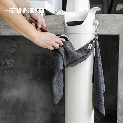 MHW-3BOMBER black hangable towel held beside its hanging attachment