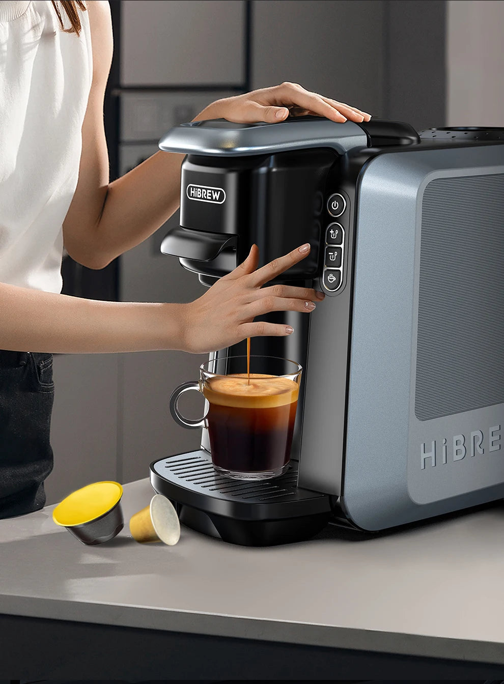 HiBREW H6 coffee maker front controls during use; cup and capsules shown are separate.