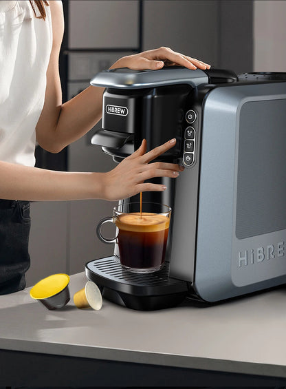 HiBREW H6 coffee maker front controls during use; cup and capsules shown are separate.