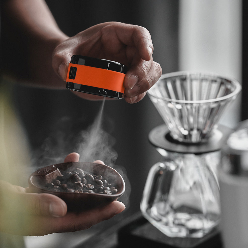 IKAPE electric coffee bean atomizer, black and orange, mist over a hand-held bowl