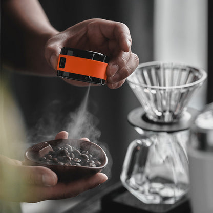 IKAPE electric coffee bean atomizer, black and orange, mist over a hand-held bowl