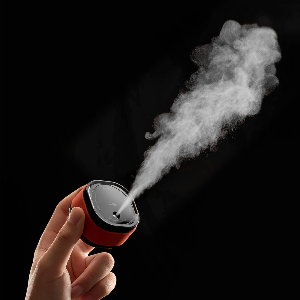 IKAPE electric coffee bean atomizer, black and orange, held upright showing spray direction