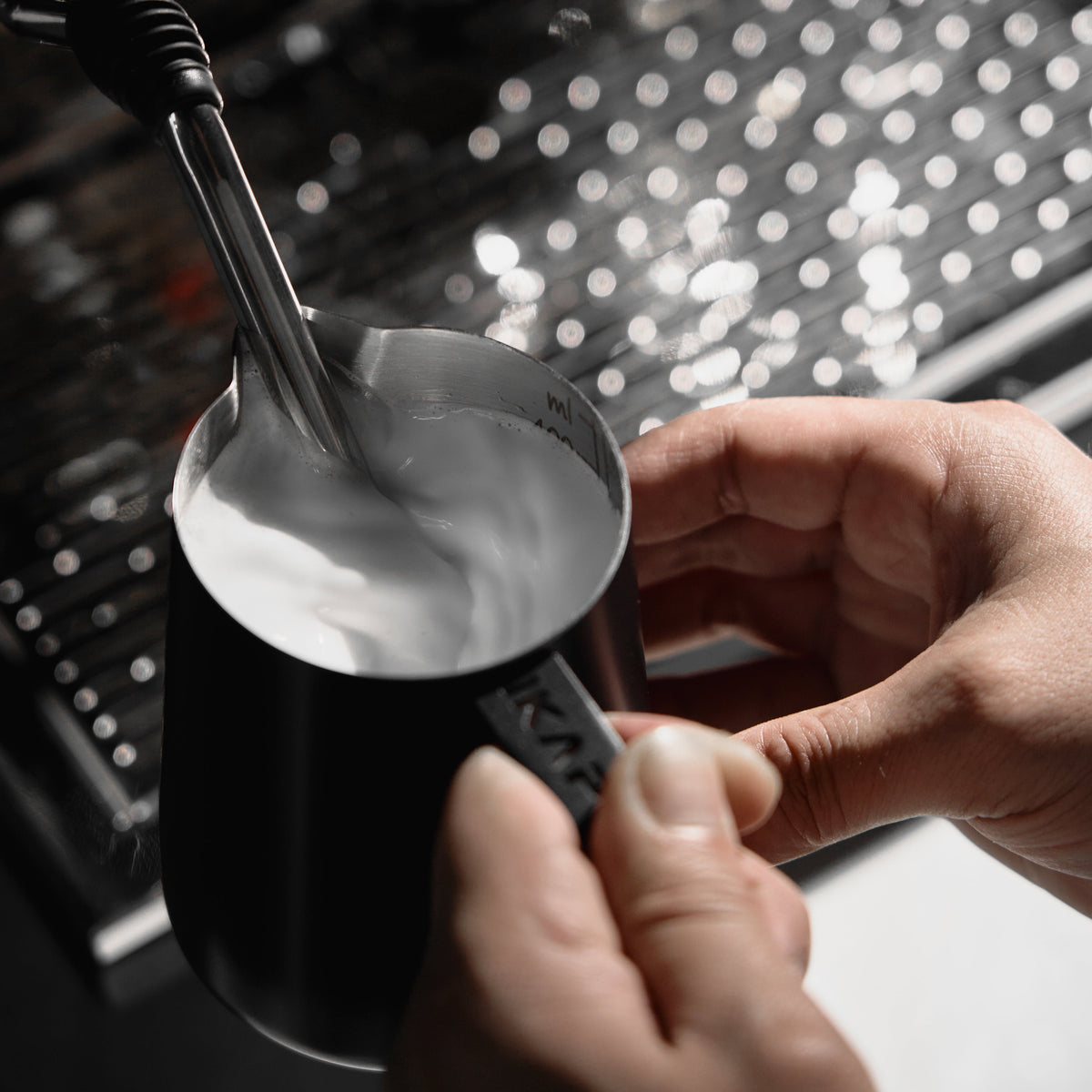 Black IKAPE hollow-handle milk pitcher steaming milk, viewed from above