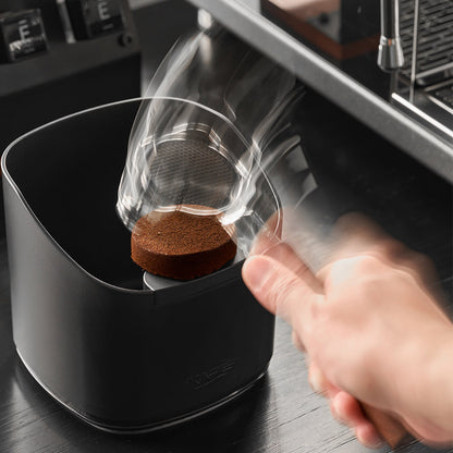 IKAPE V2 black ABS knock box in use with a portafilter; demonstration equipment excluded