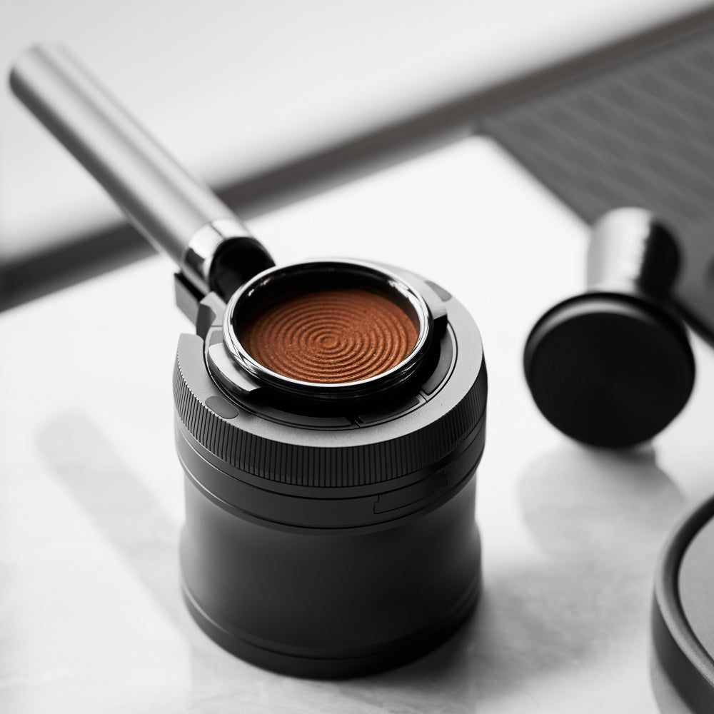 IKAPE V4 black rotary adjustable portafilter stand, manufacturer usage photograph 7; shown portafilter and preparation tools are props
